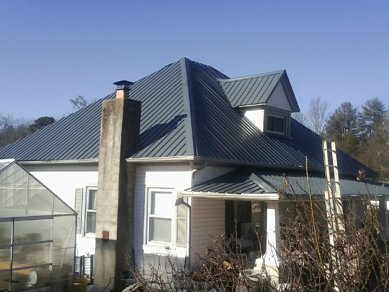 Dark blue standing seam metal roof on a white farmhouse with dormer — Slate & Tile Roof Repair by Roofing Brothers in Bloomville
