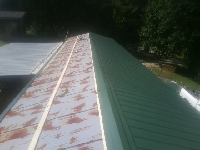 Old rusted panels beside newly installed green metal roofing — Wind Damage Roof Repair by Roofing Brothers in Bloomville