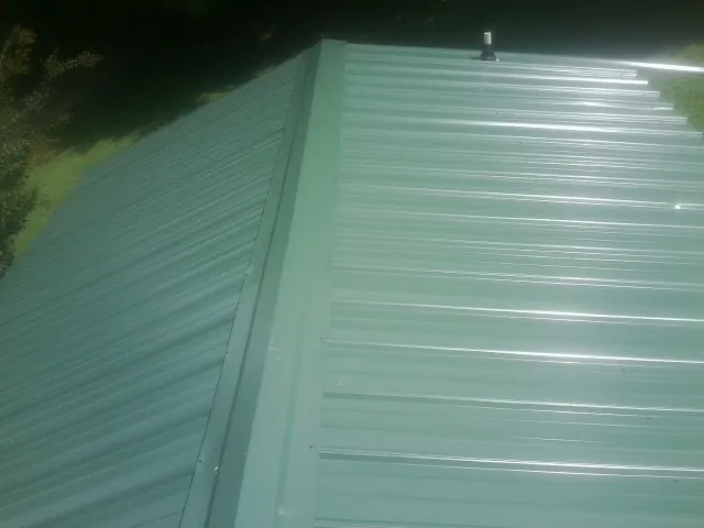 New green metal panels meeting at the ridge of a roof — Flat Roof Repair work by our crew in Bloomville