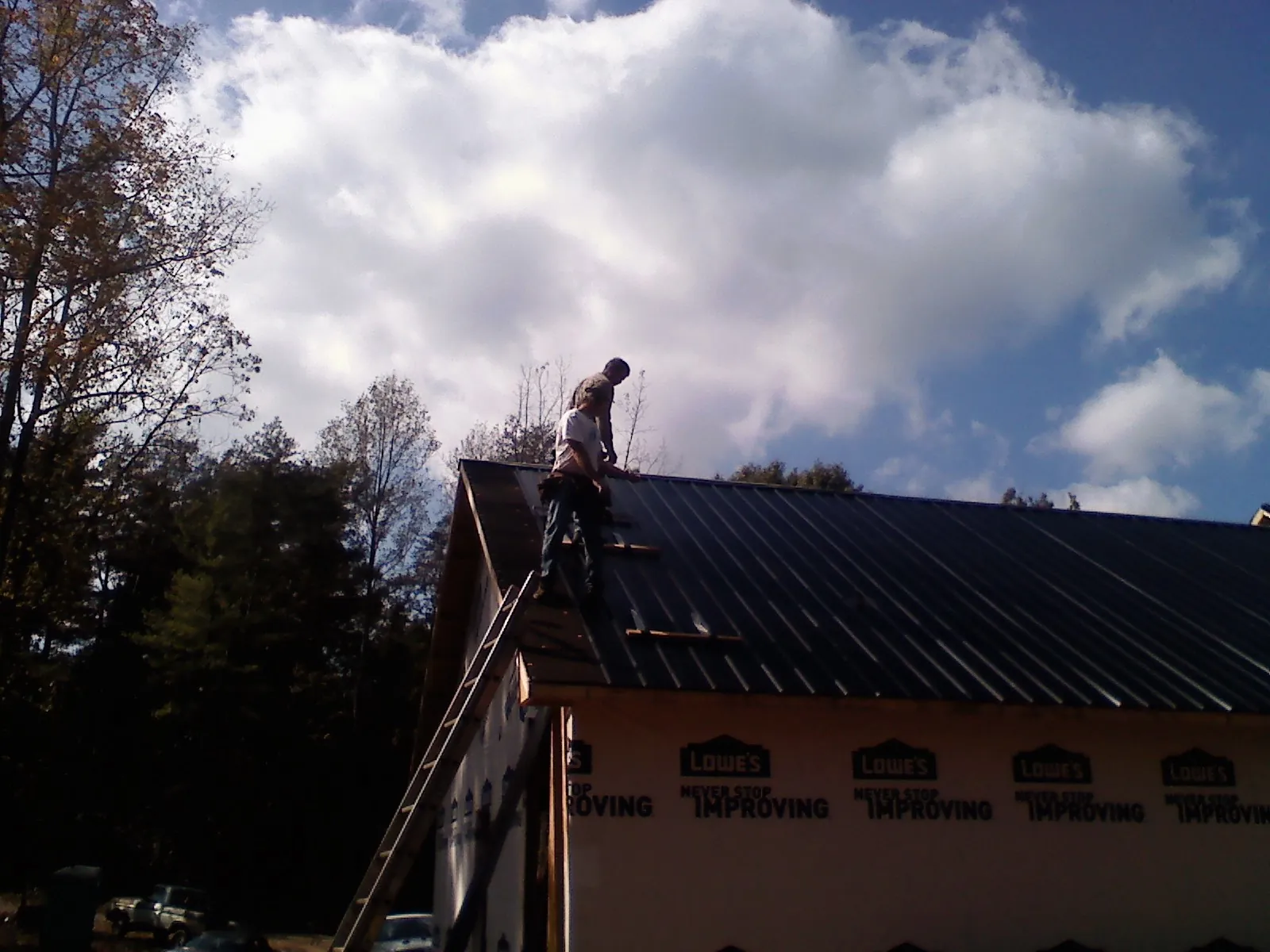 Roofer fastening dark metal panels high against a cloudy sky, from a Roof Inspection job in Bloomville