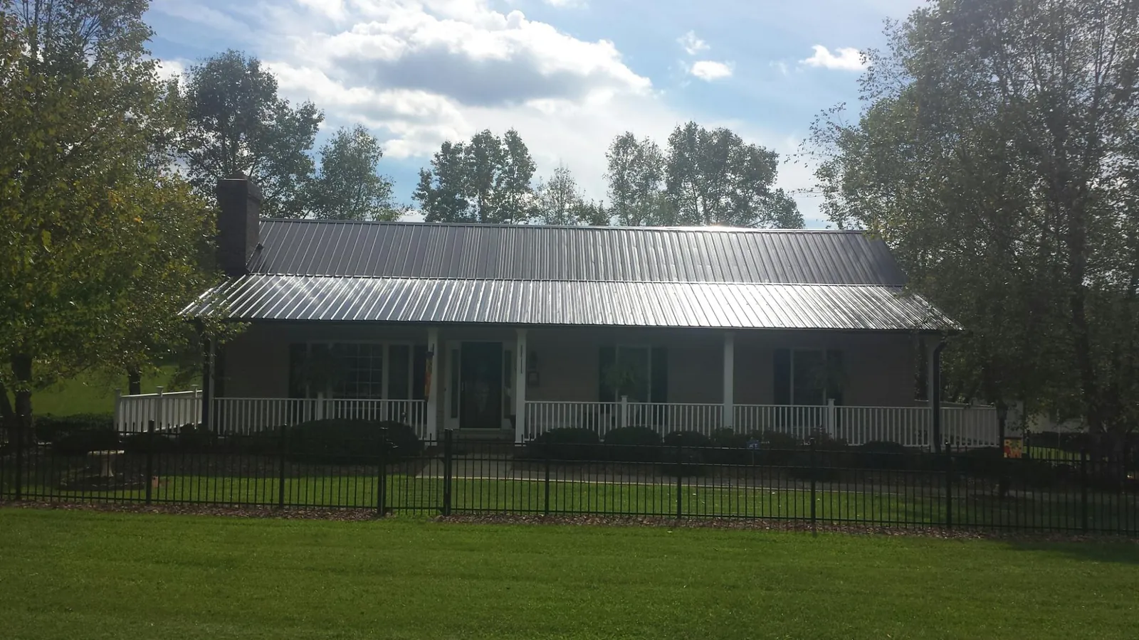 Gray metal roof on a brick ranch with a full width front porch — Gutter Guard Installation work by our crew in Bloomville