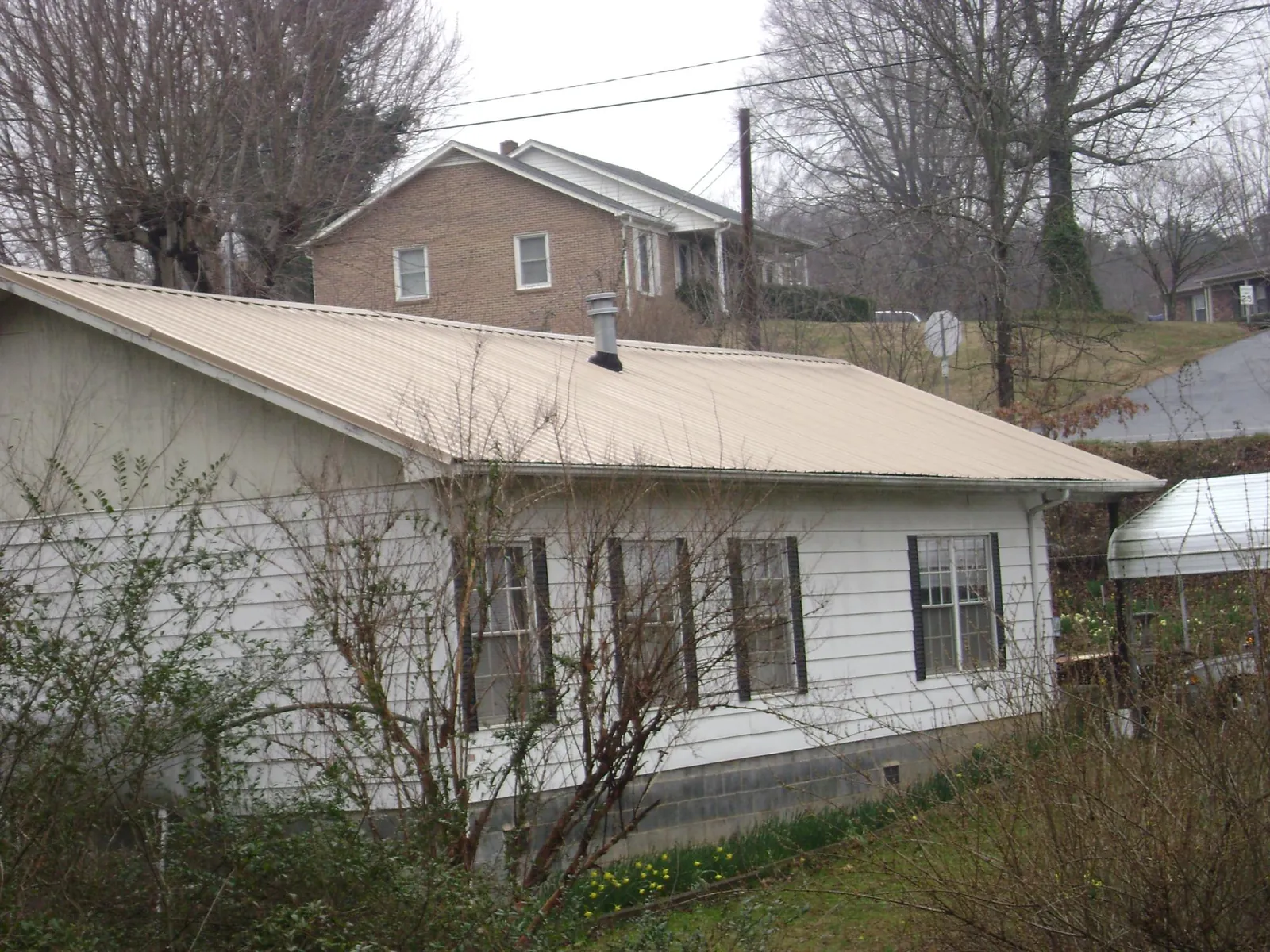 Tan metal roof on a white sided house set into a hillside — Commercial Roofing by Roofing Brothers in Bloomville
