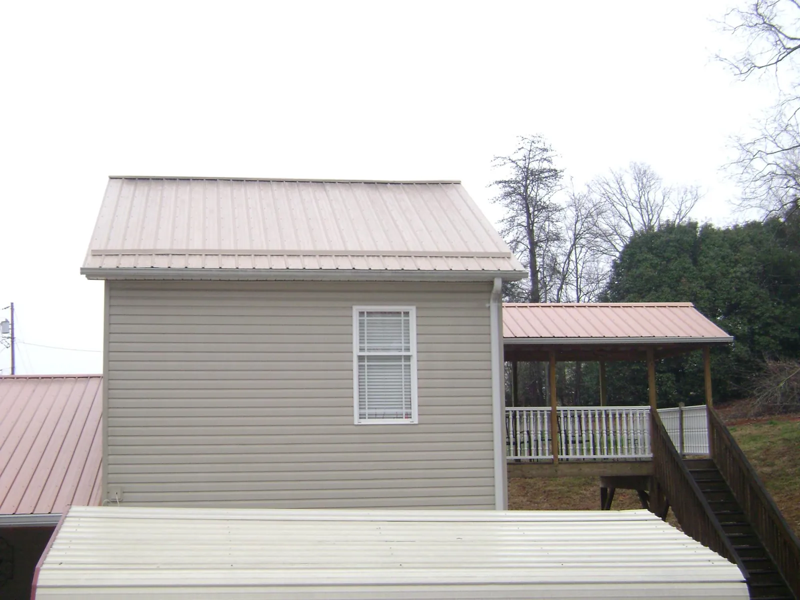 Tan metal roofs on a two story addition and attached porch, from a Roof Replacement job in Bloomville